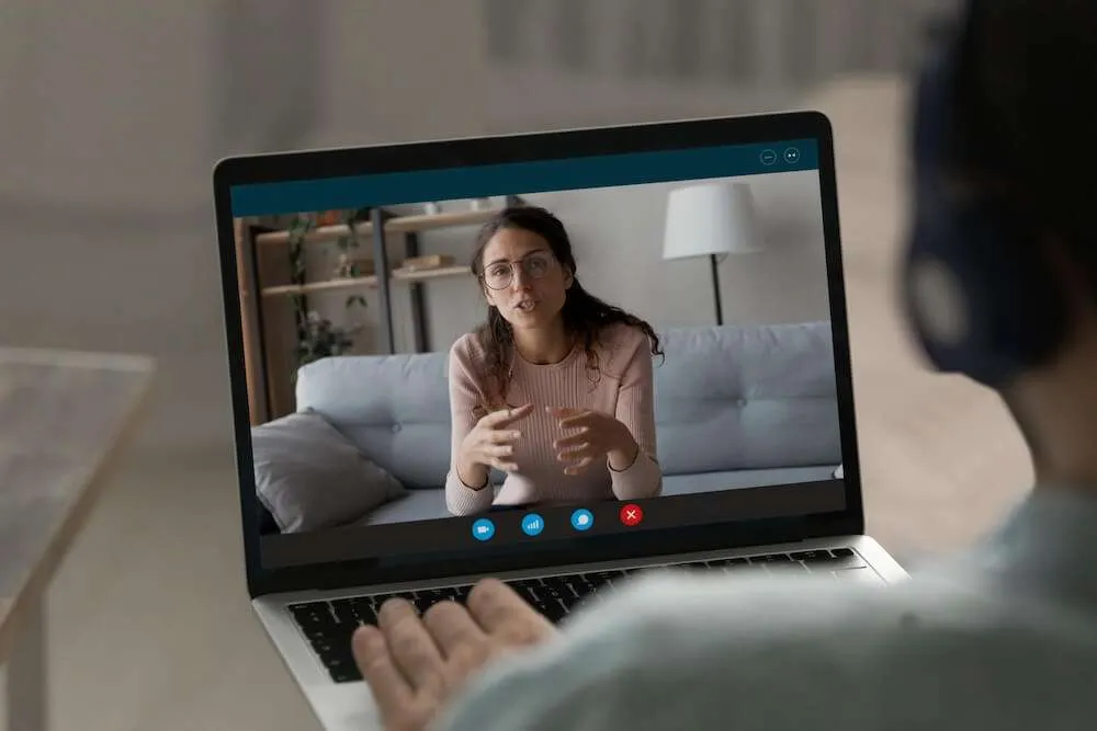 Woman with a laptop on her lap whilst on a Zoom call with another woman.