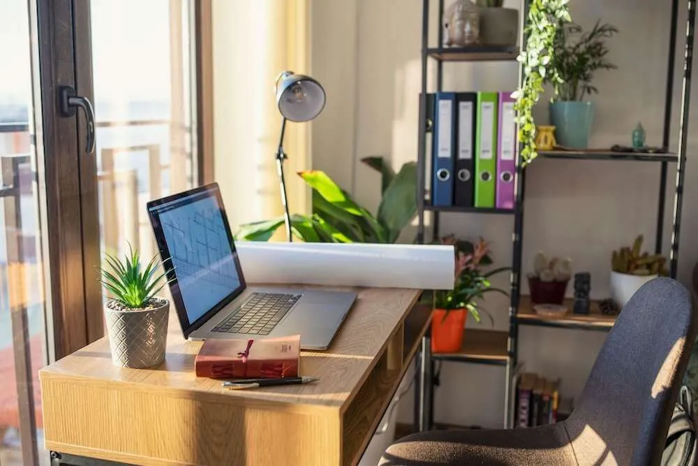A laptop is open on a desk with a bookcase in teh background