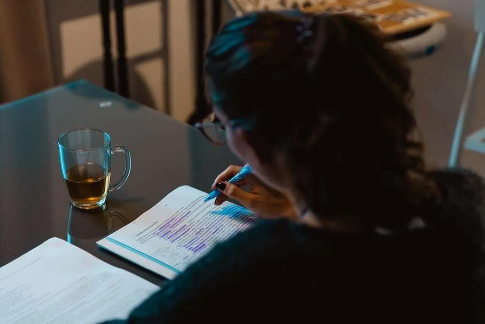 A darkened photo of a woman from behind annotating a piece of paper