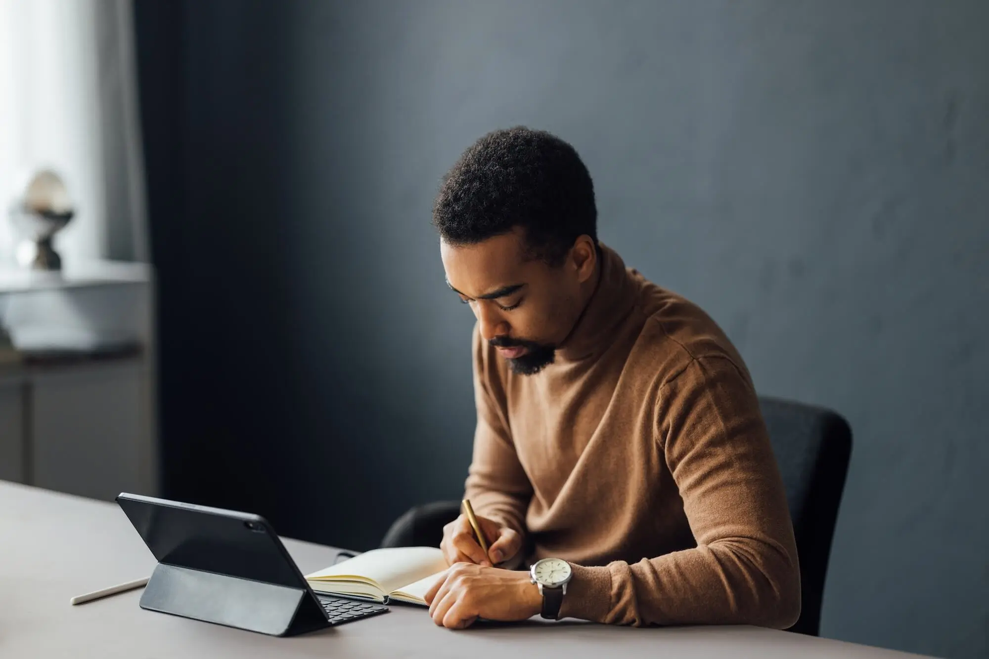 Man writing on a desk with a tablet computer open in front of him