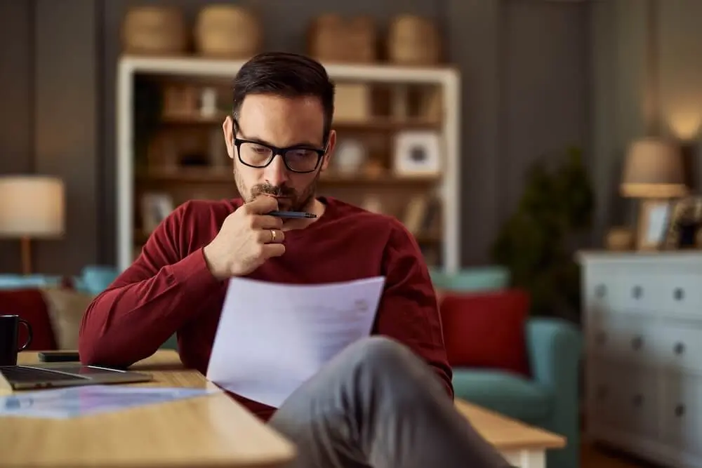 Man sitting crossed legged at a table reading a document deep in thought.