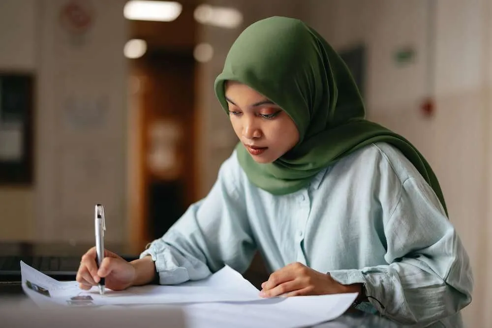 A woman holding a pen closely reads and annotates a piece of paper