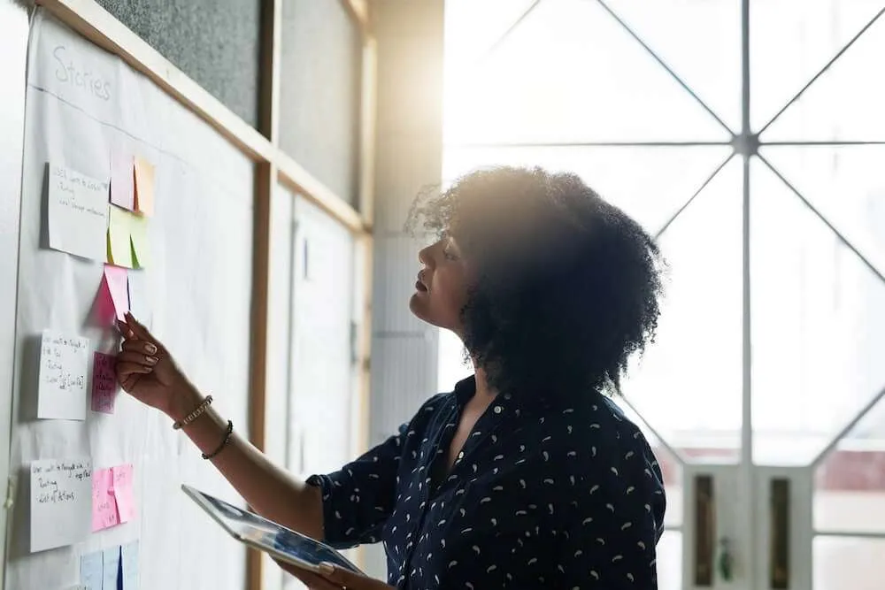 Woman standing in front of wall planner organising notes.